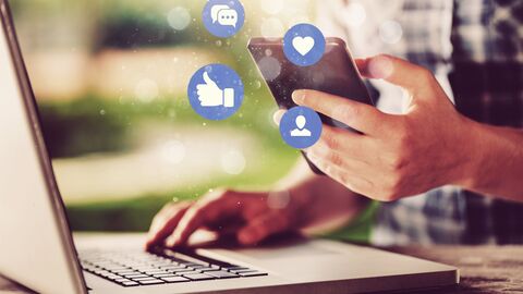 Hände tippen auf Tastatur, während Social Media Icons über Smartphone schweben Hände tippen auf Tastatur, während Social Media Icons über Smartphone schweben