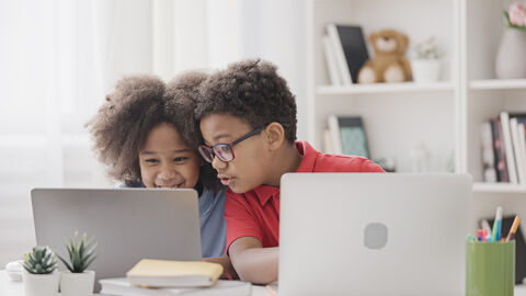 Dein Internet, mein Internet, unser Internet. Zwei Kinder sitzen mit zwei Laptops am Tisch und lachen miteinander.