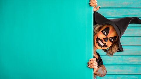 Haloween ist Gruselzeit! Kind in Hesenkostüm und schauriger Gesichtsbemalung guckt hinter einer Wand hervor und zieht eine Schreck-Grimasse