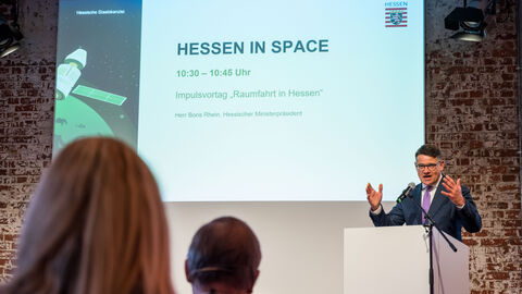 Ministerpräsident Rhein am Rednerpult, hinter ihm eine Präsentation zu "Hessen in Space"