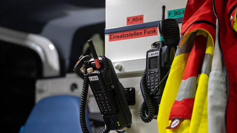 Zwei Funkgeräte von Rettungssanitätern hängen an der Wand. Daneben ebenfalls eine Jacke.