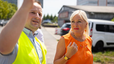 Digitalministerin Sinemus im Austausch Digitalministerin Sinemus steht mit einem Mann in gelber Weste auf einem Gelände.