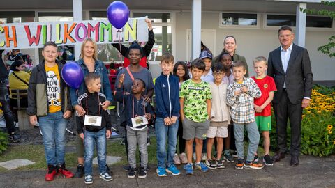 Ministerpräsident Boris Rhein nimmt an der Einschulungsfeier der Johann-Hinrich-Wichern-Schule in Frankfurt teil. Ministerpräsident Rhein steht mit Kindern und Erwachsenen vor einem Schulgebäude zum Gruppenfoto.