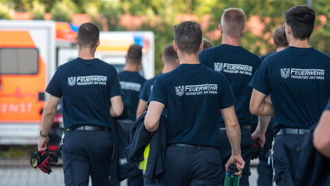 Einsatzkräfte der Feuerwehr Frankfurt am Main Mehrere Personen mit Shirts mit der Aufschrift "Feuerwehr Frankfurt am Main" laufen über ein Gelände.