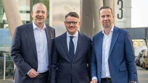 Ministerpräsident Boris Rhein schaut mit zwei weiteren Personen in die Kamera.