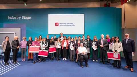 Finanzstaatssekretär Uwe Becker mit den Preisträgerinnen und Preisträgern sowie Jurymitgliedern bei der Verleihung des Hessischen Staatspreises Universelles Design 2024 am 19. November in der Messe Frankfurt. Über 20 Menschen stehen nebeneinander und halten ihre Auszeichnungen hoch.