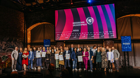 Mehrere Menschen stehen auf Bühne. Auf dem Monitor im Hintergrund steht "Hessischer Gründerpreis"