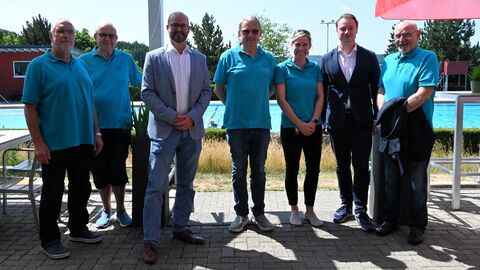 Mehrere Männer stehen vor Becken im Freibad.