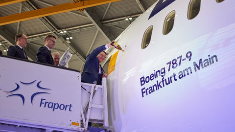 Ministerpräsident Boris Rhein tauft die neue Boeing 787-9 Dreamliner am Flughafen Frankfurt auf den Namen „Frankfurt am Main“. Ein Mann steht an einem Flugzeug und schüttet Sekt auf die Seite.