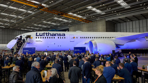 Ministerpräsident Boris Rhein macht in seiner Rede die enge Partnerschaft mit der Lufthansa deutlich. Das Flugzeug steht im Hangar und davor stehen über 50 Personen und schauen es an.