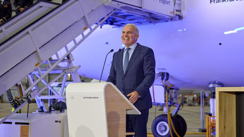 Carsten Spohr, Vorstandsvorsitzender der Deutschen Lufthansa AG, stellt in seiner Rede die Herausforderungen für die Lufthansa und die Luftverkehrswirtschaft heraus. Ein Mann steht an einem Rednerpult. Im Hintergrund ist das Flugzeug.
