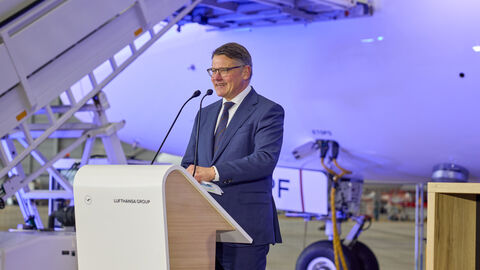 Ministerpräsident Boris Rhein spricht sich für ein umfassendes Entlastungspaket für die Luftverkehrswirtschaft aus. Ein Mann steht an einem Rednerpult. Im Hintergrund ist das Flugzeug.