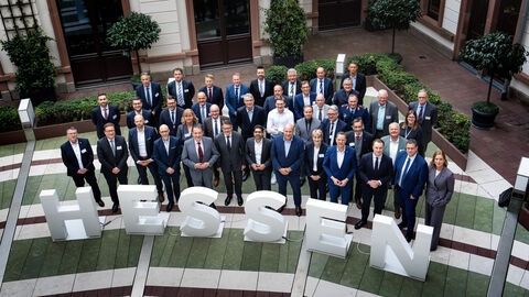 Rüstungsgipfel in Wiesbaden 2025 Über 30 Personen stehen in 3 Reihen nebeneinander in einem Innenhof und schauen nach oben in die Kamera. Vor ihnen sind 1 Meter hohe Buchstaben platziert, die das Wort "Hessen" ergeben.