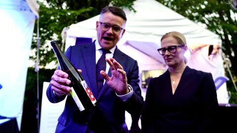 Ministerpräsident Boris Rhein hält eine Flasche Wein in der Hand. Neben ihm steht seine Frau.