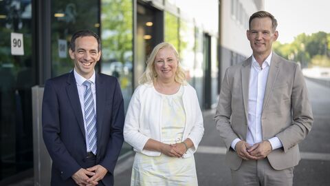 Drei Personen stehen vor einem Eingang.