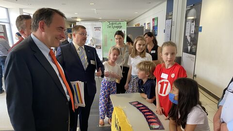 Kultusminister Lorz feiert 13. Hessischen Demokratietag mit Schülerinnen und Schülern in Bensheim Kultusminister Lorz steht vor einem Stand von Schülerinnen und Schülern und lächelt sie an.