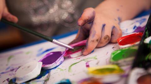 Malendes Kind Hand eines Kindes mit Wasserfarbe verschmiert und Pinsel in der Hand an einem Farbkasten