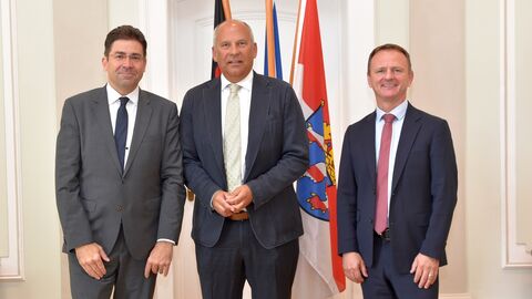Besuch Regierungspräsidium Darmstadt Regierungspräsident Prof. Dr. Jan Hilligardt , Innenminister Roman Poseck und Vizepräsident Dr. Stefan Fuhrmann (v.l.n.r.) stehen nebeneinander, im Hintergrund stehen Flaggen.