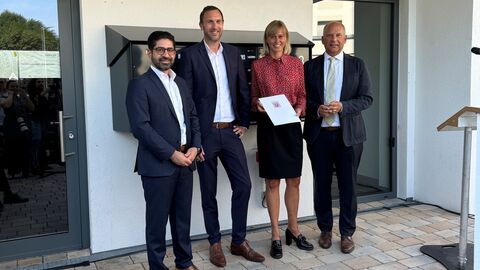 Siegelübergabe Sicher Wohnen in Hessen Wirtschaftsminister Kaweh Mansoori, Dr. Axel Tausendpfund (Vorstand des Verbands der Südwestdeutschen Wohnungswirtschaft, VdW südwest), Mirja Dorny (Geschäftsführerin Baugesellschaft Hanau), Innenminister Roman Poseck (v. l. n. r.) stehen nebeneinander vor einem Haus.
