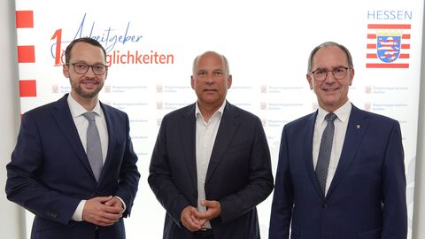 Antrittsbesuch RP Gießen Drei Männer im Anzügen blicken in Kamera. Im Hintergrund sieht man das Hessen-Logo