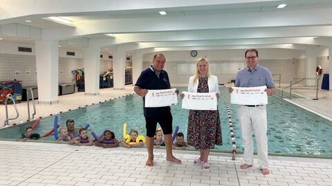 Sportministerin Diana Stolz hat sich in der Schwimmhalle der Frankfurter Carl-Schurz- Schule bei Michael Ulmer, Sportlicher Leiter des Schwimmzentrums (links) und Frank Scheuerer, Teamleiter Marketing FNP (rechts) über das Programm „Seepferdchen - Frankfurt lernt Schwimmen“ informiert Sportministerin Diana Stolz steht in einem Schwimmbad zwischen zwei Männern.
