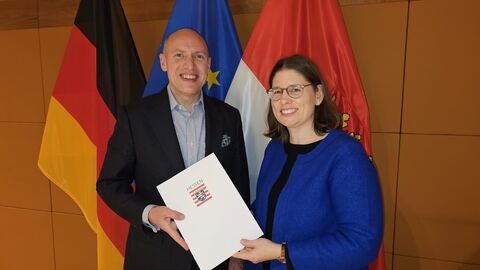 Staatminister Manfred Pentz und Dr. Katharina Brauer bei der Übergabe der Ernennungsurkunde Ein Mann und eine Frau stehen nebeneinander und halten gemeinsam eine Urkunde hoch.