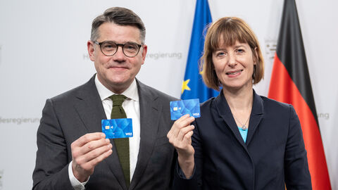 Ministerpräsident Boris Rhein und Sozialministerin Heike Hofmann stehen nebeneinander und halten jeweils eine blaue Geldkarte hoch.