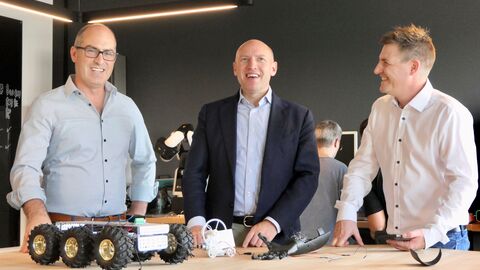 Minister Pentz steht gemeinsam mit zwei weiteren Personen an einem Tisch auf dem einzelne elektrische Bauteile liegen.