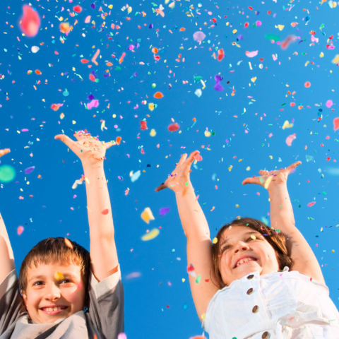 Hurra, wir feiern Zwei fröhliche Kinder werfen buntes Konfetti in die Luft.